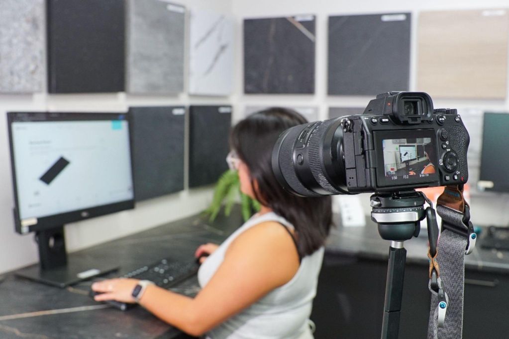 A professional mirrorless camera captures a Conversion
Marketing Content Creator and Social Media Manager working
on a computer in a showroom with tile samples, illustrating
a Kiwi business creating authentic content and searchable
metadata for answer
engines.